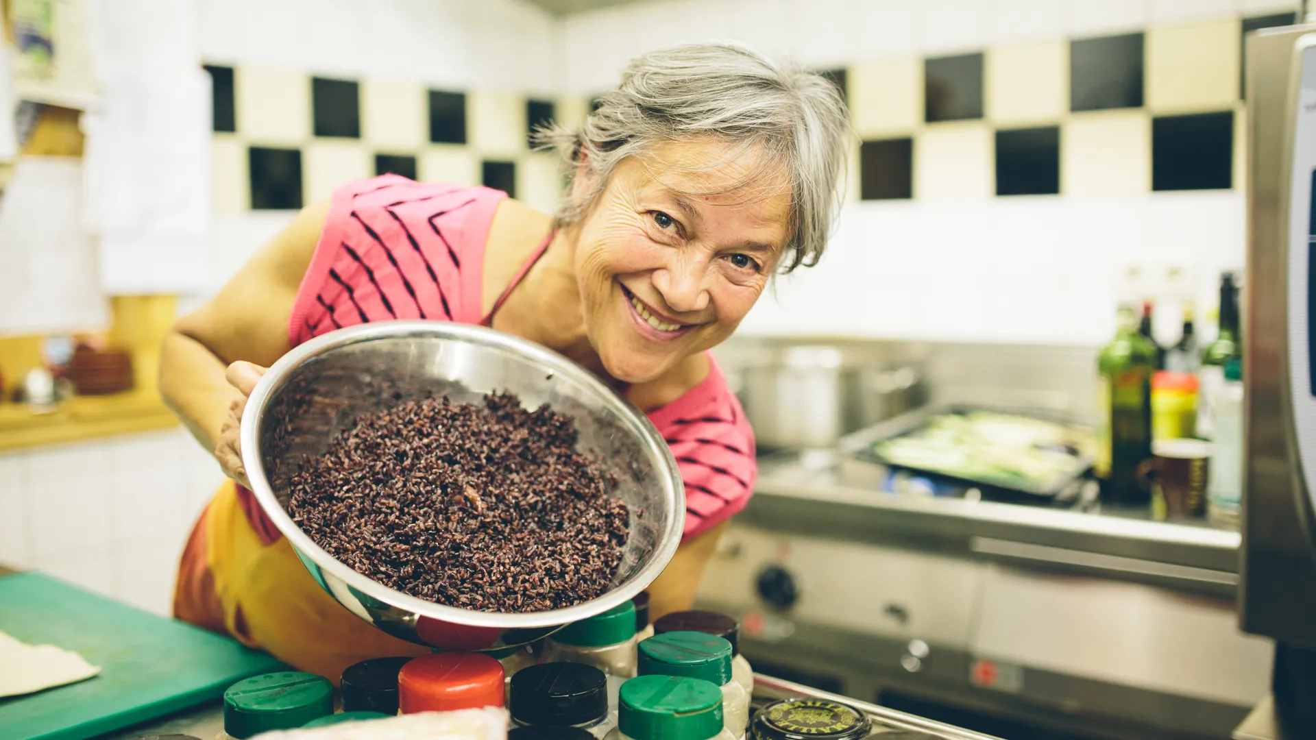 Vrouw toont schaal met zwarte rijst in keuken.