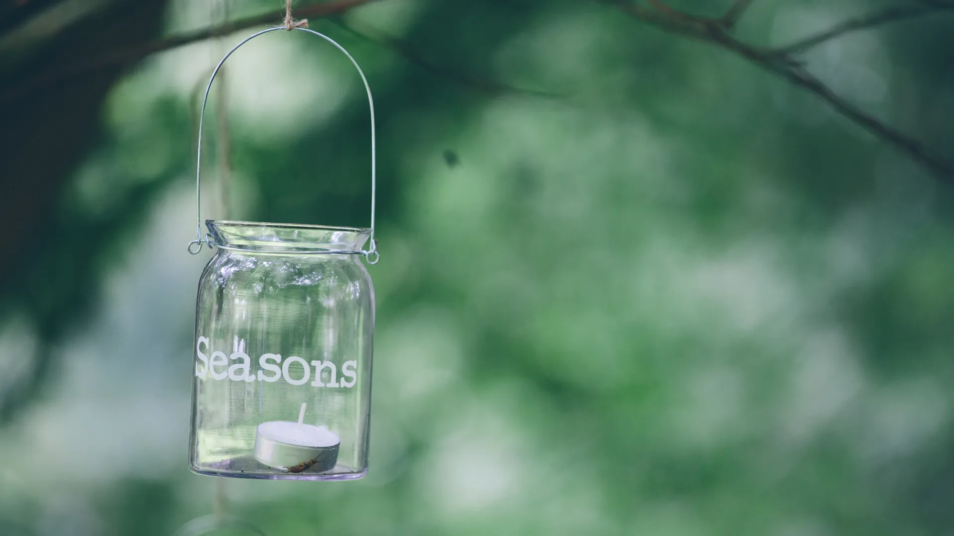 Hangende glazen pot met kaars, 'Seasons' erop.
