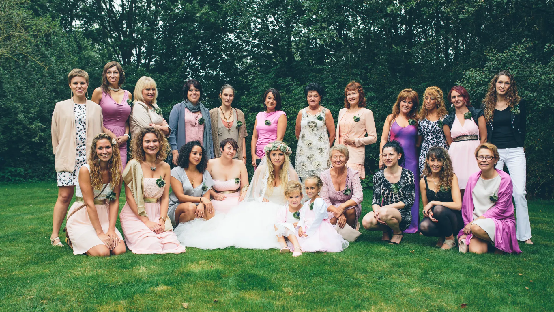Grote groep vrouwen poseert buiten, bruiloftskledij.