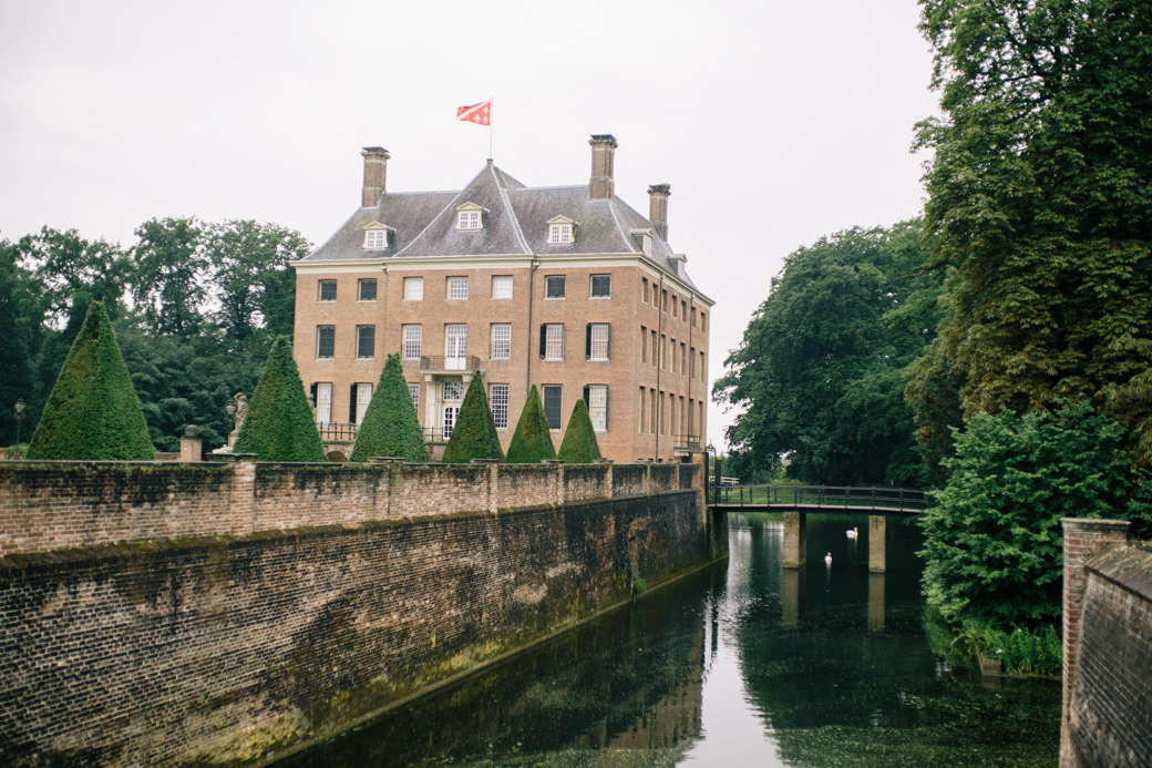 Oud kasteel met gracht en vlag op zonnige dag.