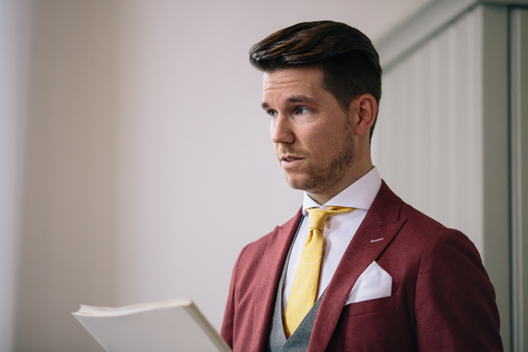 Man in rood pak met gele stropdas, leest tekst.