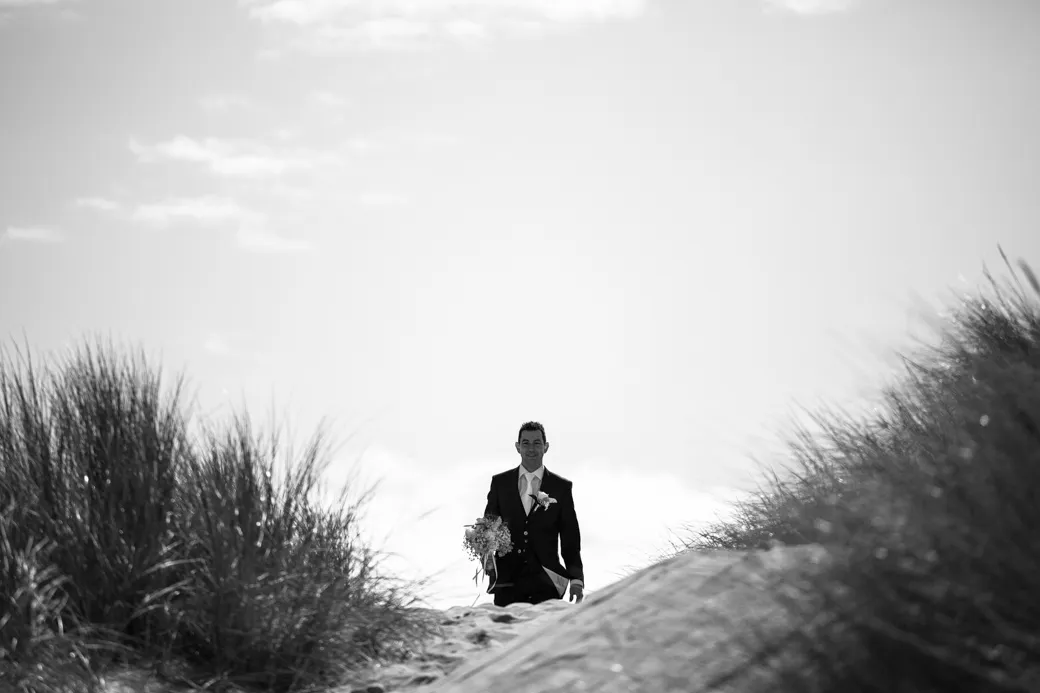 Man in pak loopt door duinen met bloemen