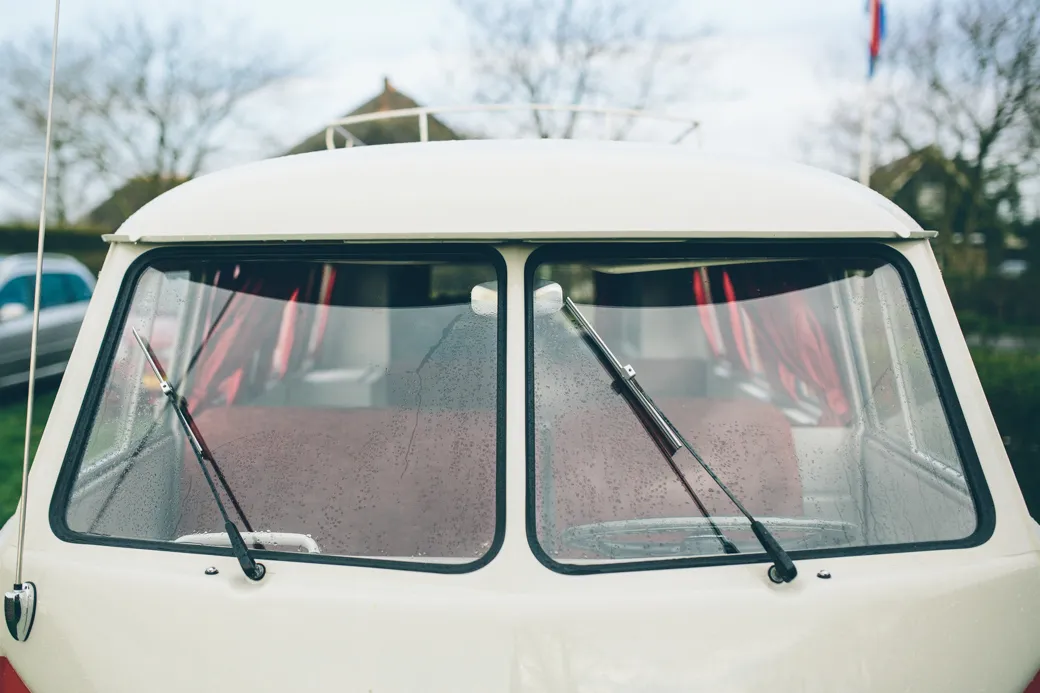 Voorruit van oude bus met ruitenwissers en regendruppels.