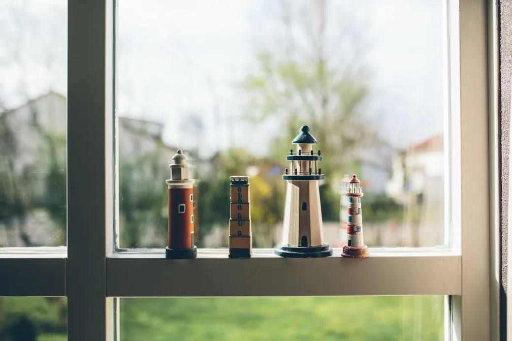 Miniatuur vuurtorens op binnenraam met uitzicht buiten.