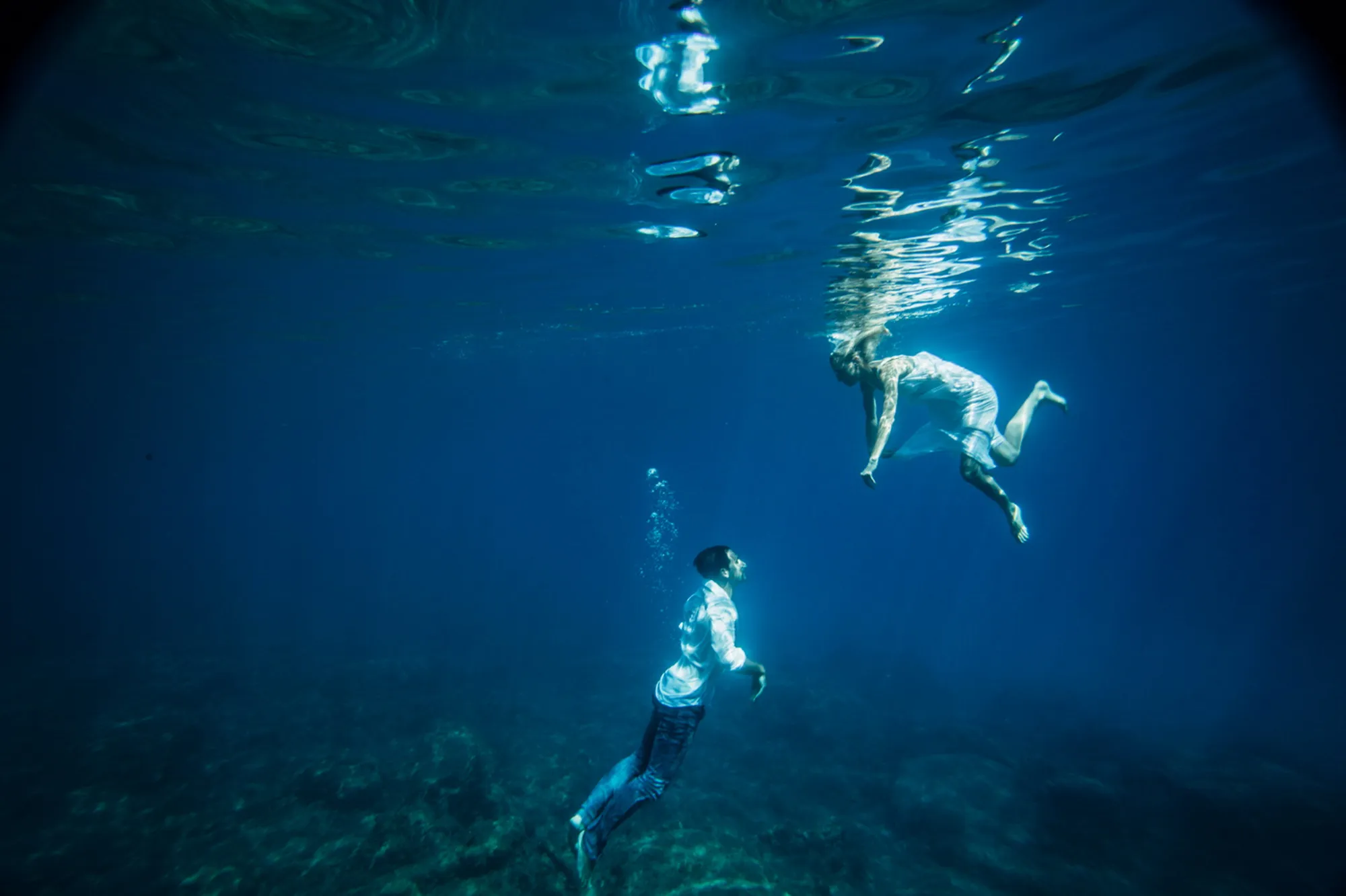 Twee mensen zwemmen onder water in blauwe oceaan.